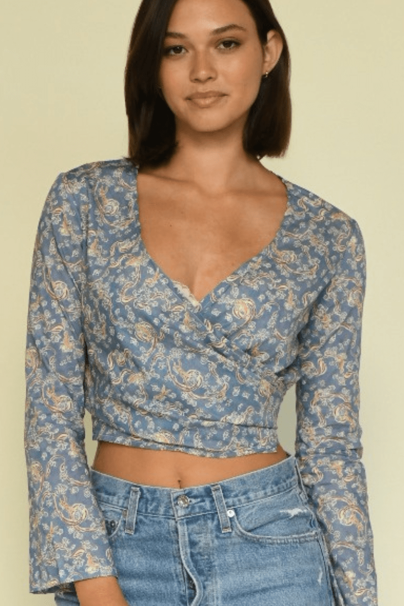 Woman wearing a blue wrap top with tan floral print and long sleeves paired with light blue denim jeans.