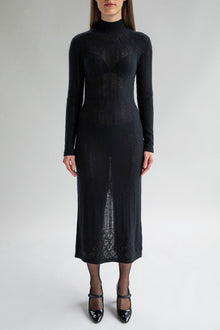 Woman wears the Margot Dress in black, featuring a lace pointelle pattern in soft cashmere showcasing a fitted silhouette.