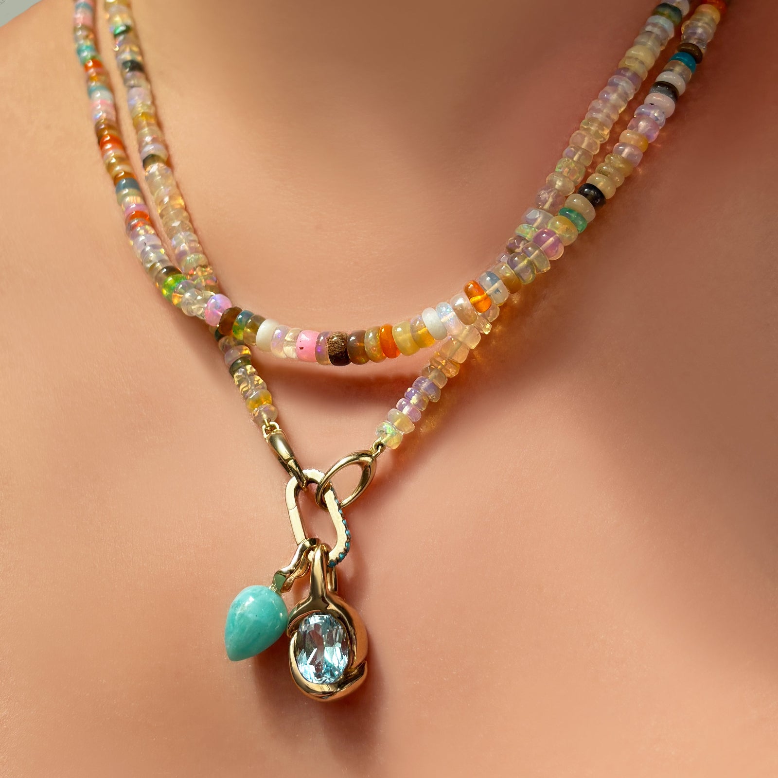Natural multi faceted opal necklace layered with mermaid disco opal necklace with a charm lock and amazonite drop charm and blue topaz molten knot charm hanging from it.