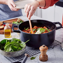 Black Dutch oven filled with stew, spinach, and sour cream, being stirred in a modern kitchen.