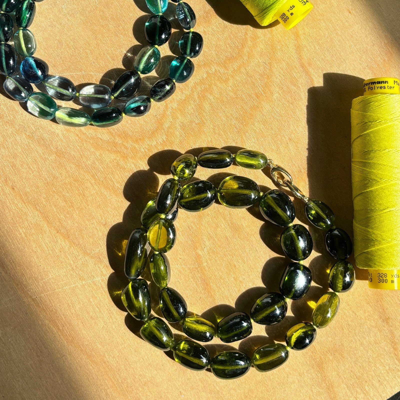 Shimmering beaded nugget bracelets with shades of green, yellow, and olive 
 and blue on a gold lobster clasp on surface.