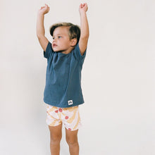 Child wearing blue t-shirt and white swim trunk with red and yellow palm leaf print.