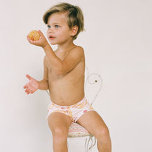 Child wearing white swim trunks with colorful palm tree and citrus fruit print.