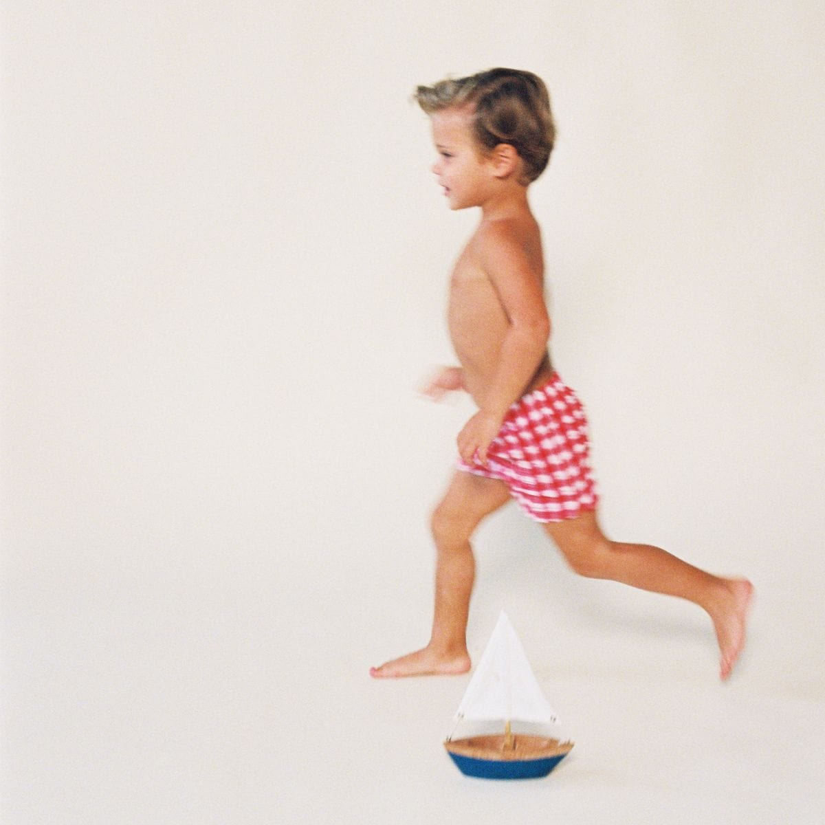 Child wearing red and white gingham swim trunks, shown in profile running pose.