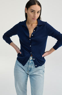 Woman wearing a navy blue cardigan over a white shirt with light blue jeans on a plain background