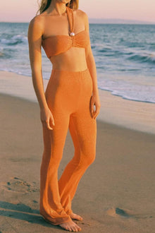 Woman wearing orange sparkle flare pants with matching bandeau top on beach.
