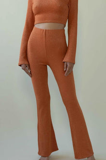 Rust-colored flared pants with high waist and sparkle texture, shown with matching crop top.