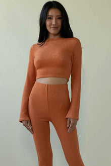 Rust-colored sparkle knit crop top with long sleeves and cutout waist detail, paired with matching high-waisted pants.