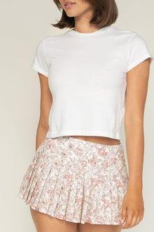 Pleated tennis skirt with pink and cream floral pattern paired with white short-sleeve t-shirt.